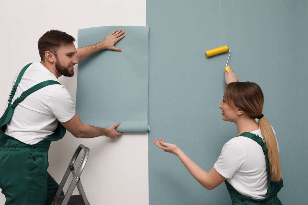 Een persoon brengt vliesbehang aan op een muur met behulp van een behangborstel, illustrerend het proces van het aanbrengen van vliesbehang.