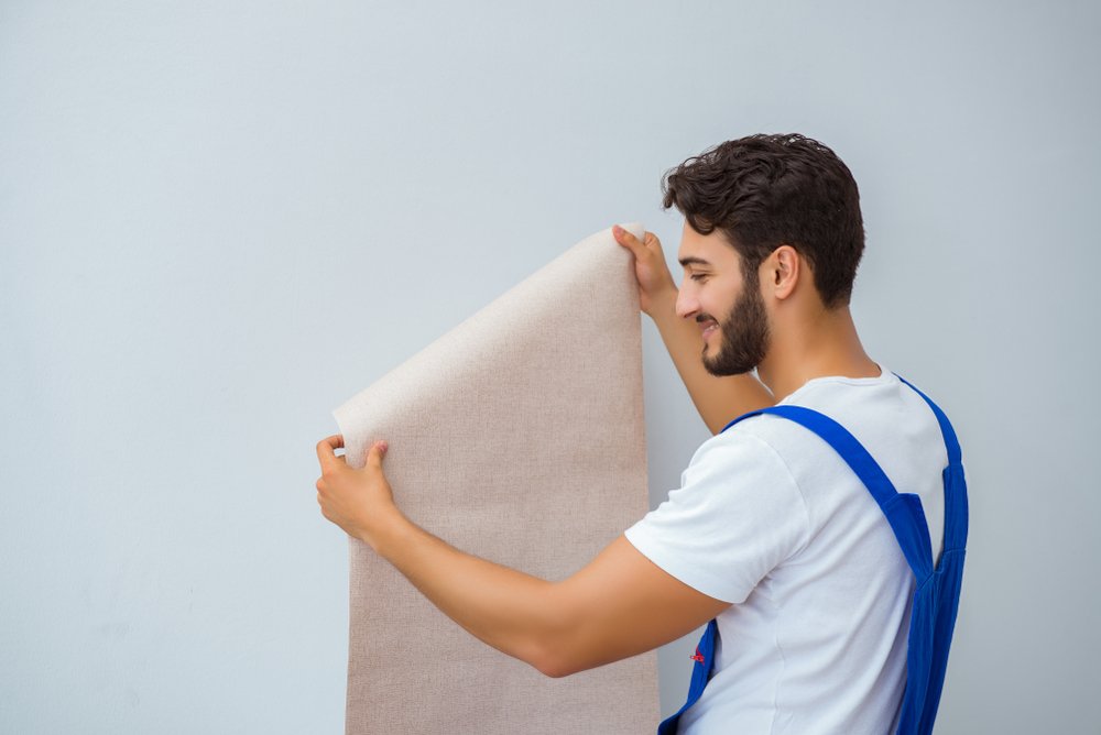 Een persoon plaatst vliesbehang op een muur met behulp van een behangborstel, illustrerend het proces van het behangen van vliesbehang.