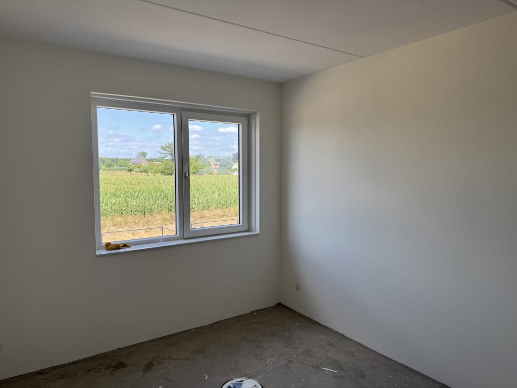 Lege nieuwbouwkamer met gladde, lichte wanden en een groot raam