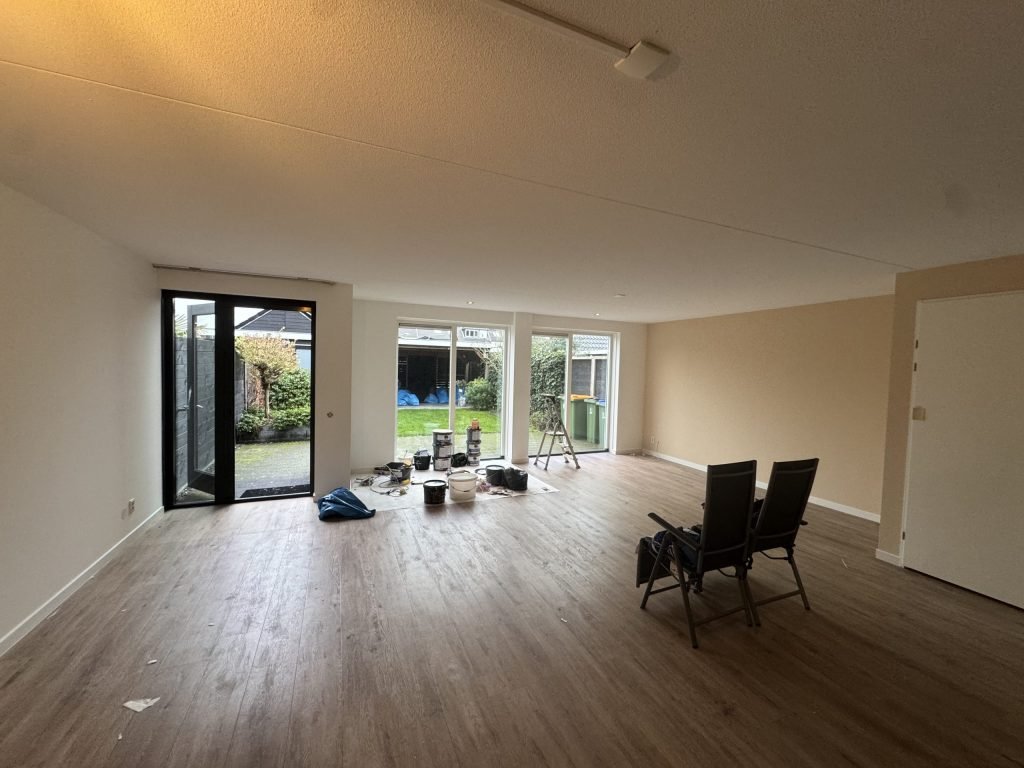Ruime woonkamer met lichte, gesausde wanden en tuindeuren, tijdens de afwerking