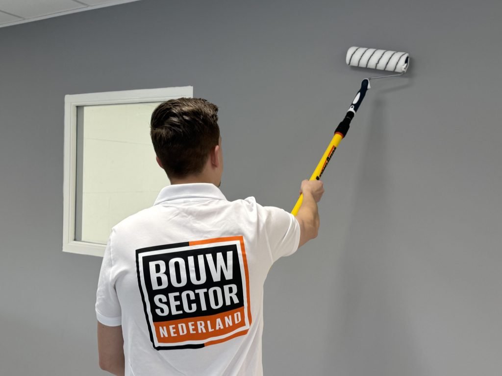 Vakman van Bouwsector Nederland saust een grijze wand met een roller aan een steel