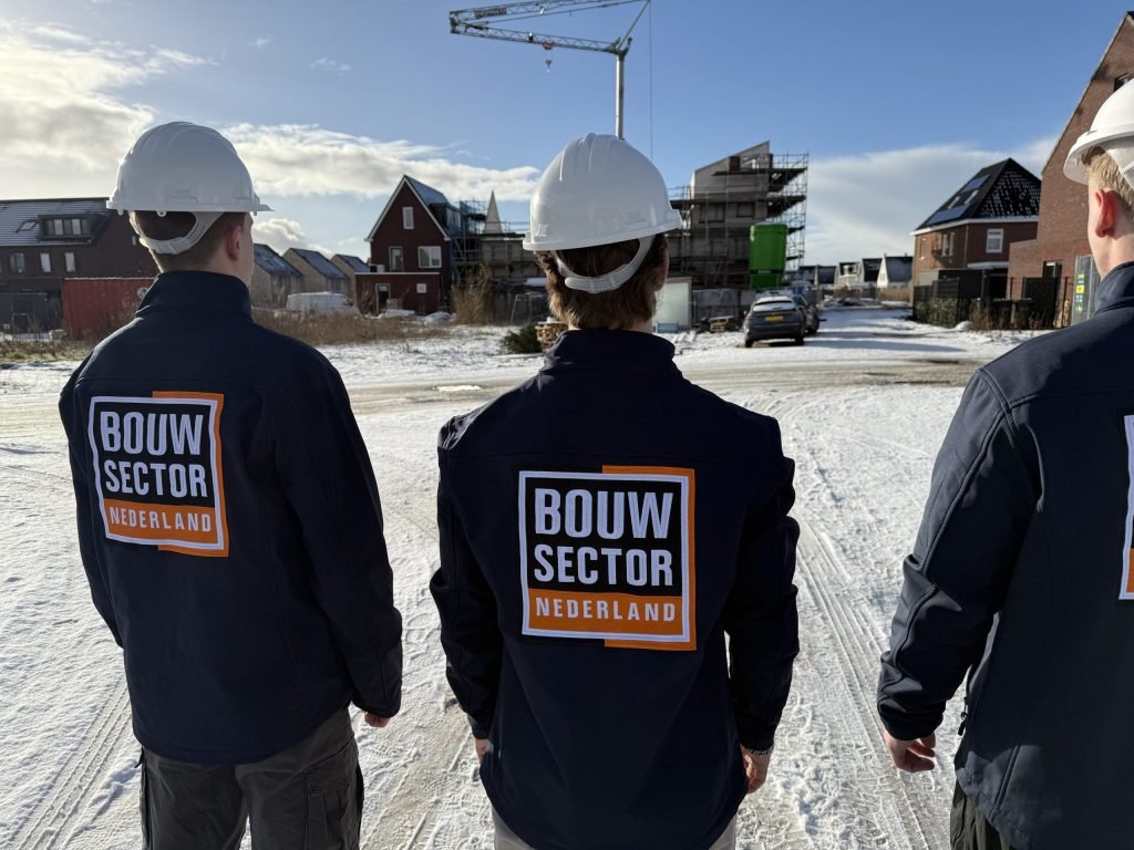 Drie vakmensen van Bouwsector Nederland met witte helm op een besneeuwde nieuwbouwlocatie
